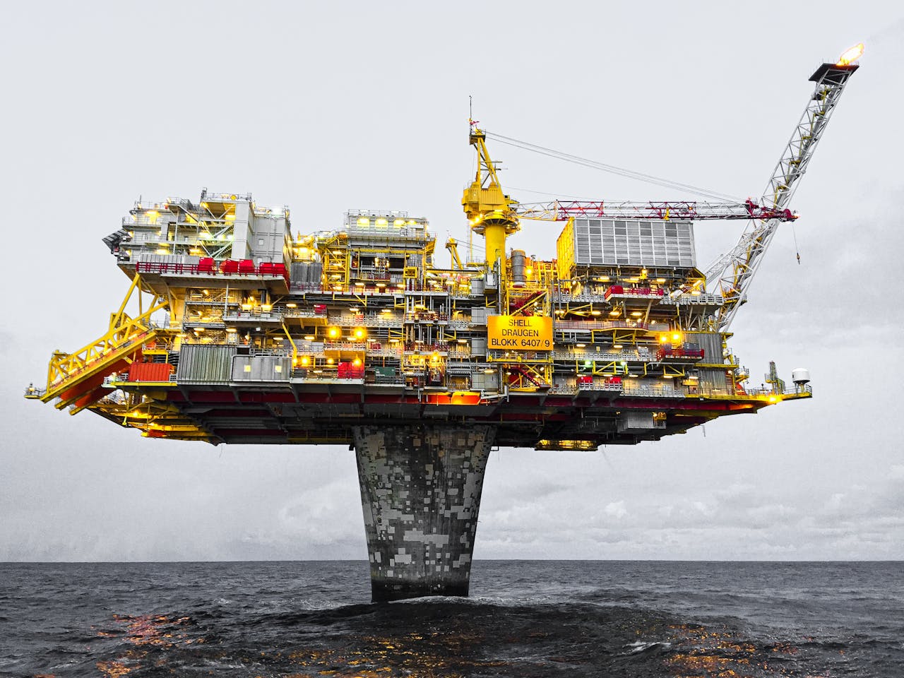 why-choose-us A well-lit offshore oil platform against a cloudy sky in Norway's waters.